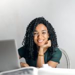 Happy ethnic woman sitting at table with laptop