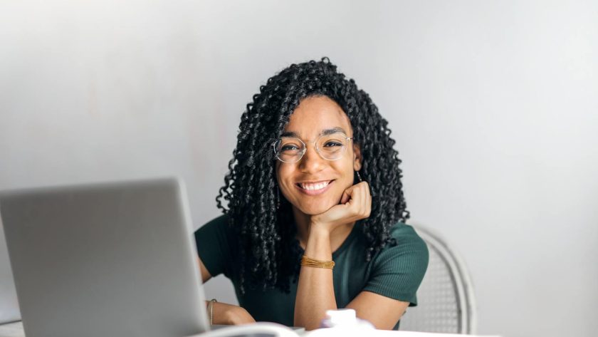 Happy ethnic woman sitting at table with laptop